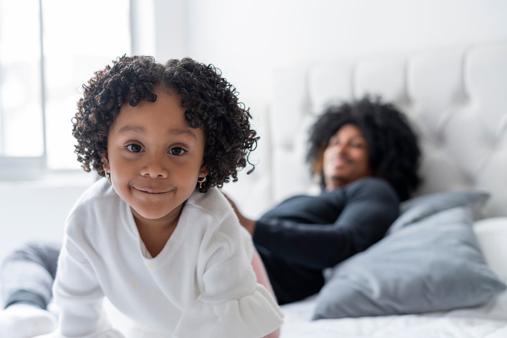 curly-kid-on-the-bed-smiling-while-looking-at-camera