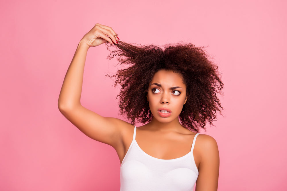 Woman with hair struggles holding up a strand of hair and looking frustrated