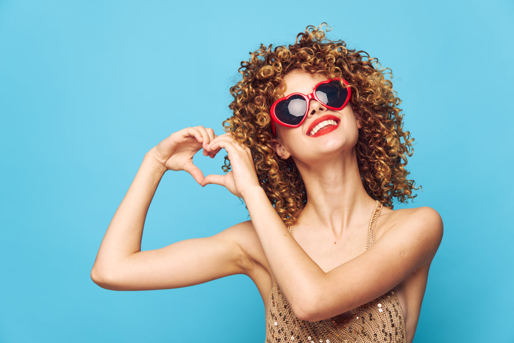 woman with naturally curly hair expressing love wearing heart shaped sunglasses