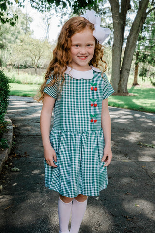 girl outside wearing green gingham dress with berry buttons