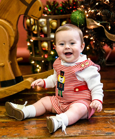 A baby boy in a red houndstooth shortall
