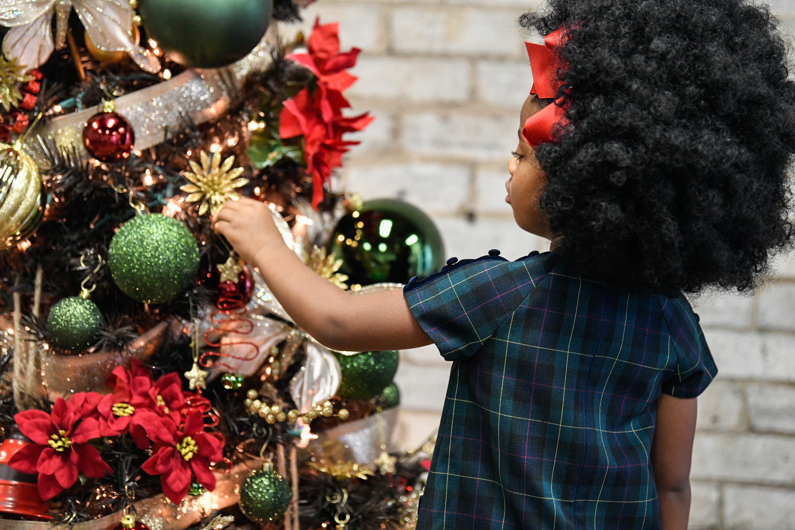 young girl decorating a tree in a classic gbventurespub tartan dress