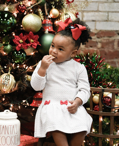 young girl eating a cookie in a white dress with small flowers and red bows