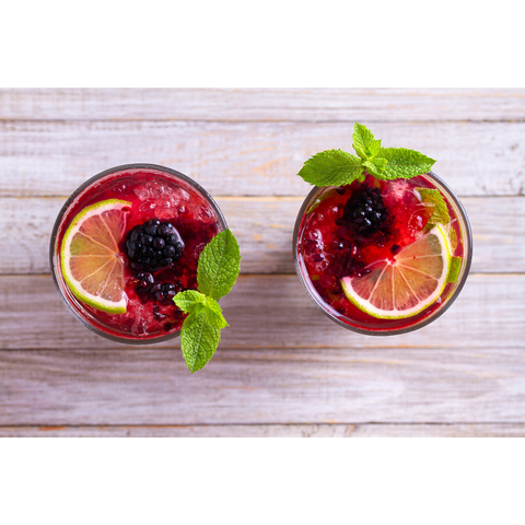 Airplane view of 2 drinks with cranberry juice, blackberries, and half a slice of lime.