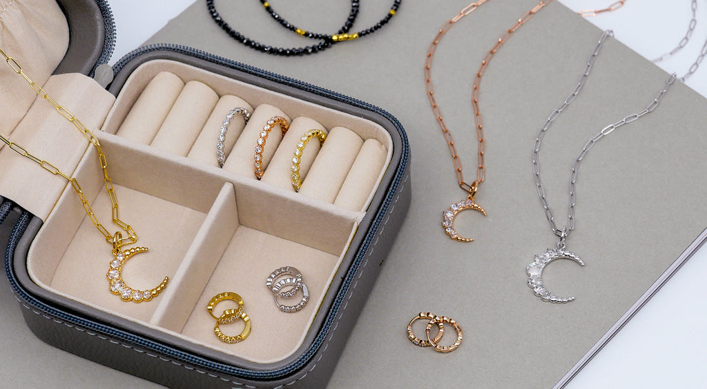 The Crescent Pendant, Bezel Band, Zelda Huggies, and Noir Black Diamond Bracelet placed around small jewelry case