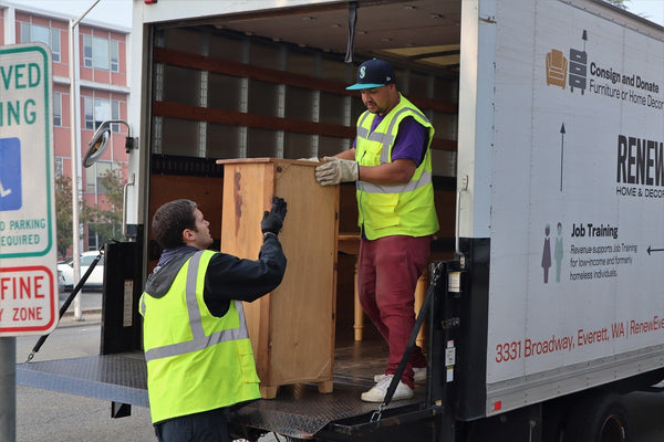 Photo of two men unloading furniture from the back of a delivery truck.