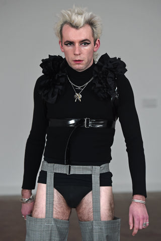 LULA LAORA AW21 Getty Images, menswear model wears a black ruffled harness over a long sleeved black t-shirt and black underwear. He also wears  houndstooth garter trousers. 