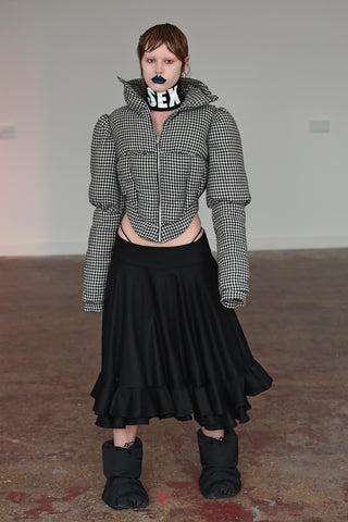 LULA LAORA AW21 Getty Images, womenswear model has blue lips and short hair. She wears a houndstooth puffer jacket and a black midi skirt with black puffer shoes