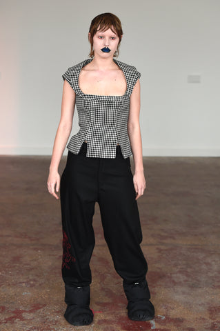 LULA LAORA AW21 Getty Images, womenswear model wears sleeveless houndstooth top with two small front slits and a U shape neckline. She also wears black oversized trousers and puffy shoes. 