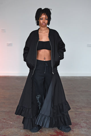 LULA LAORA AW21 Getty Images, womenswear model wears black bralette top, joggers/sweatpants with a white lady print, and a black bomber jacket with two layers. 