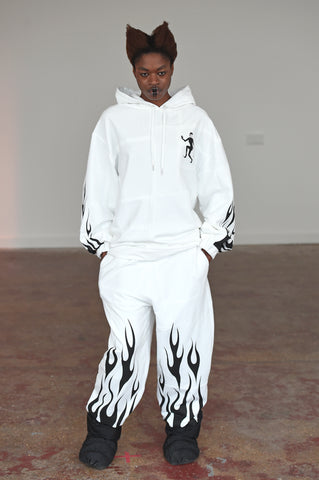 LULA LAORA AW21 Getty Images,womenswear model wears white tracksuit and black puffy shoes. The hoodie has a black evil lady logo and flames on the sleeves and hem of the trousers. 