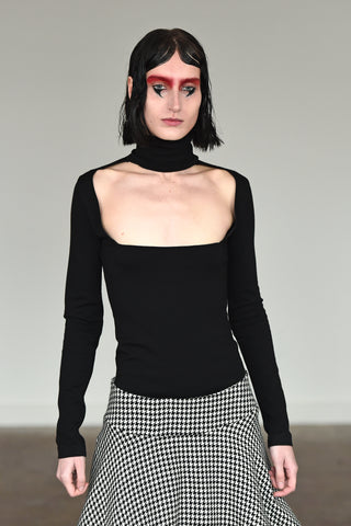 LULA LAORA AW21 Getty Images, womenswear model wears a fitted black top with a high neck and a cut-out neckline. Also wears a houndstooth skirt. 