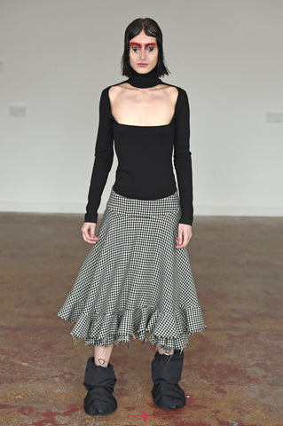 LULA LAORA AW21 Getty Images, womenswear model wears a fitted black top with a high neck and a cut-out neckline. Also wears a houndstooth midi skirt and black puffer shoes. 