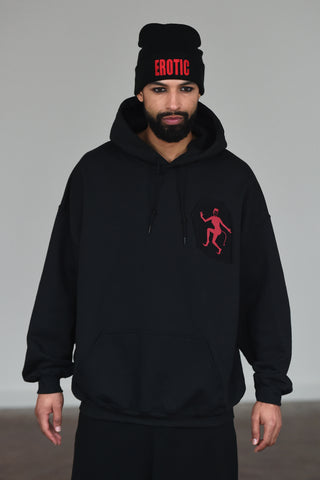 LULA LAORA AW21 Getty Images, menswear model wears a black beanie with the words erotic in red. the hoodie is black with a Red Devil lady logo, he also wears black sweatpants or joggers. 