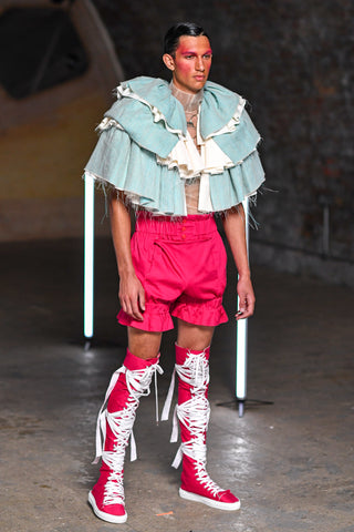 Lula Laora runway Getty pink eyebrows, cape ruffled, light blue cape, fuchsia shorts, fuchsia high top sneakers