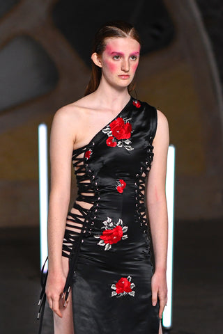 Lula Laora runway Getty pink eyebrows, asymmetrical neckline, dress, black with red flowers. Lace up sides, long dress