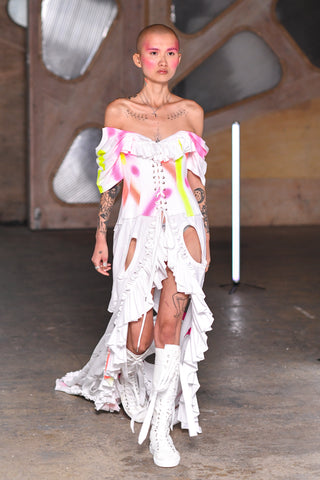 Lula Laora runway Getty pink eyebrows, long white dress with cut-outs and neon pink and yellow patterns. ruffled opening at the front, exposed shoulders, 