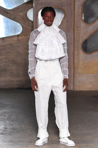 Lula Laora runway Getty pink eyebrows, white mesh long sleeved top with ruffled bib, white sneakers and white high-waisted trousers. 