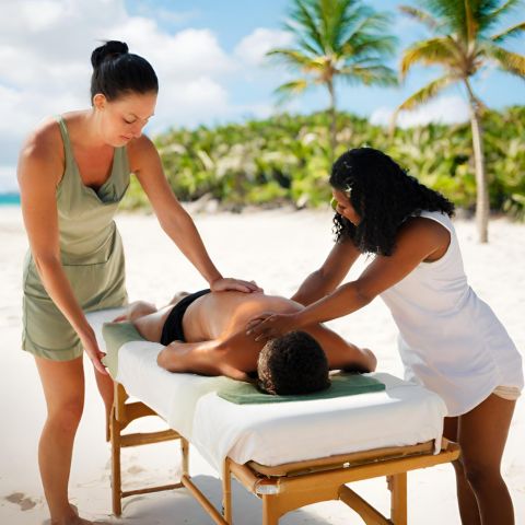 A couple receiving Lomi Lomi massage on a tropical beach.