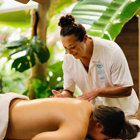 A massage therapist preforming a lumi lumi massage on a client in a tropical setting.