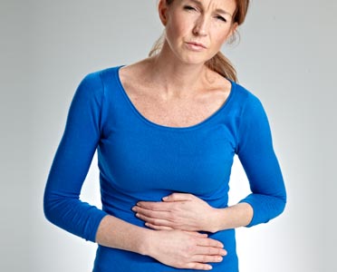 A woman wearign a blue shirt who looks to be in discomfort and is holding her stomach