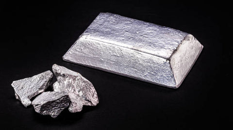 An image showing a solid silver-colored aluminum bar alongside several raw aluminum chunks against a dark background, highlighting the processed and natural forms of aluminum.