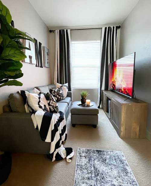cozy tv lounge with dark couch and striped blanket in front of a flat-screen TV on a TV stand