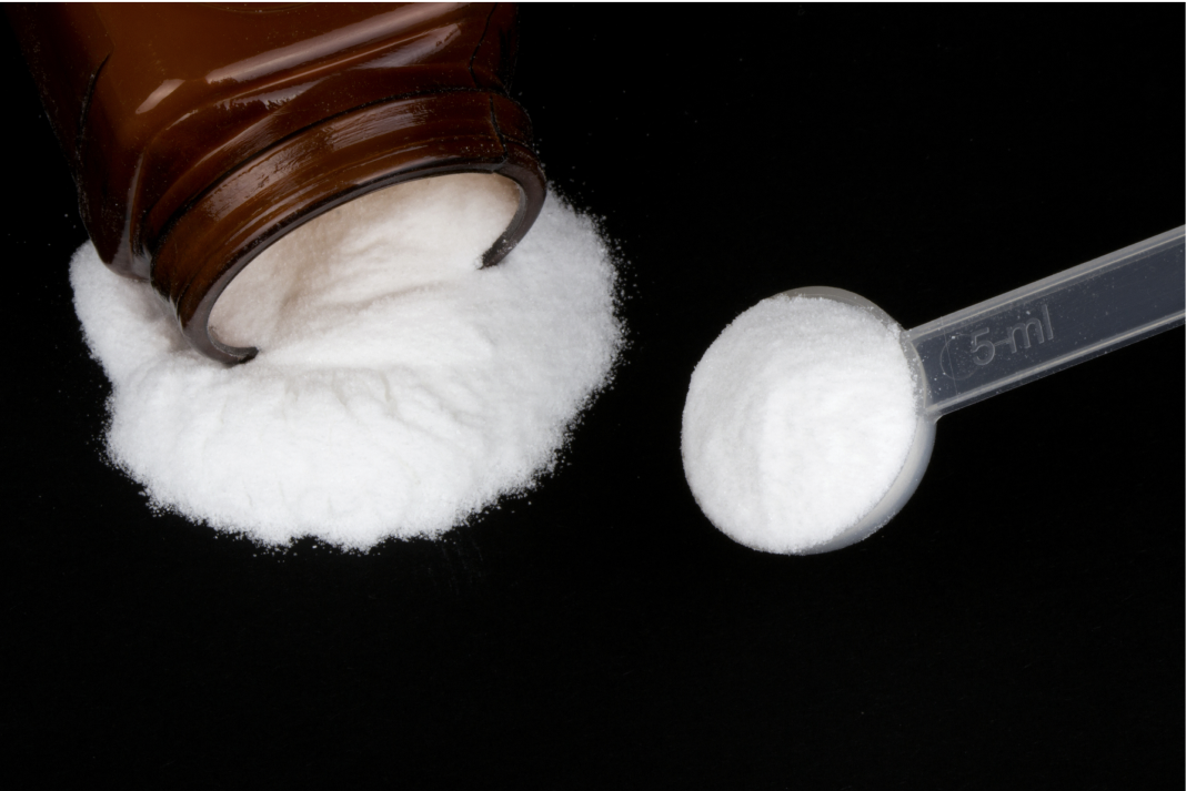 Brown bottle of white powder, with some spilled and a measuring spoon filled.