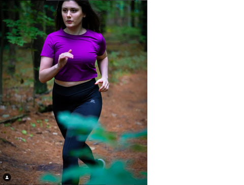 Woman running in the woods wearing purple crop top and black leggings