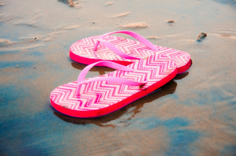  A pair of pink flip-flops laying on the sand at a beach.
