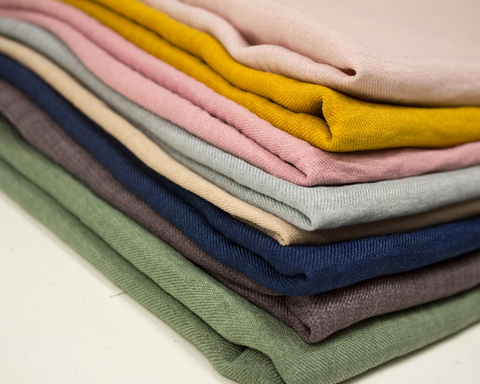 A stack of different types of fabrics in several colors. 