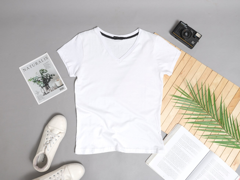 A white t-shirt, pair of sneakers, and a book lying on a grey backdrop. 