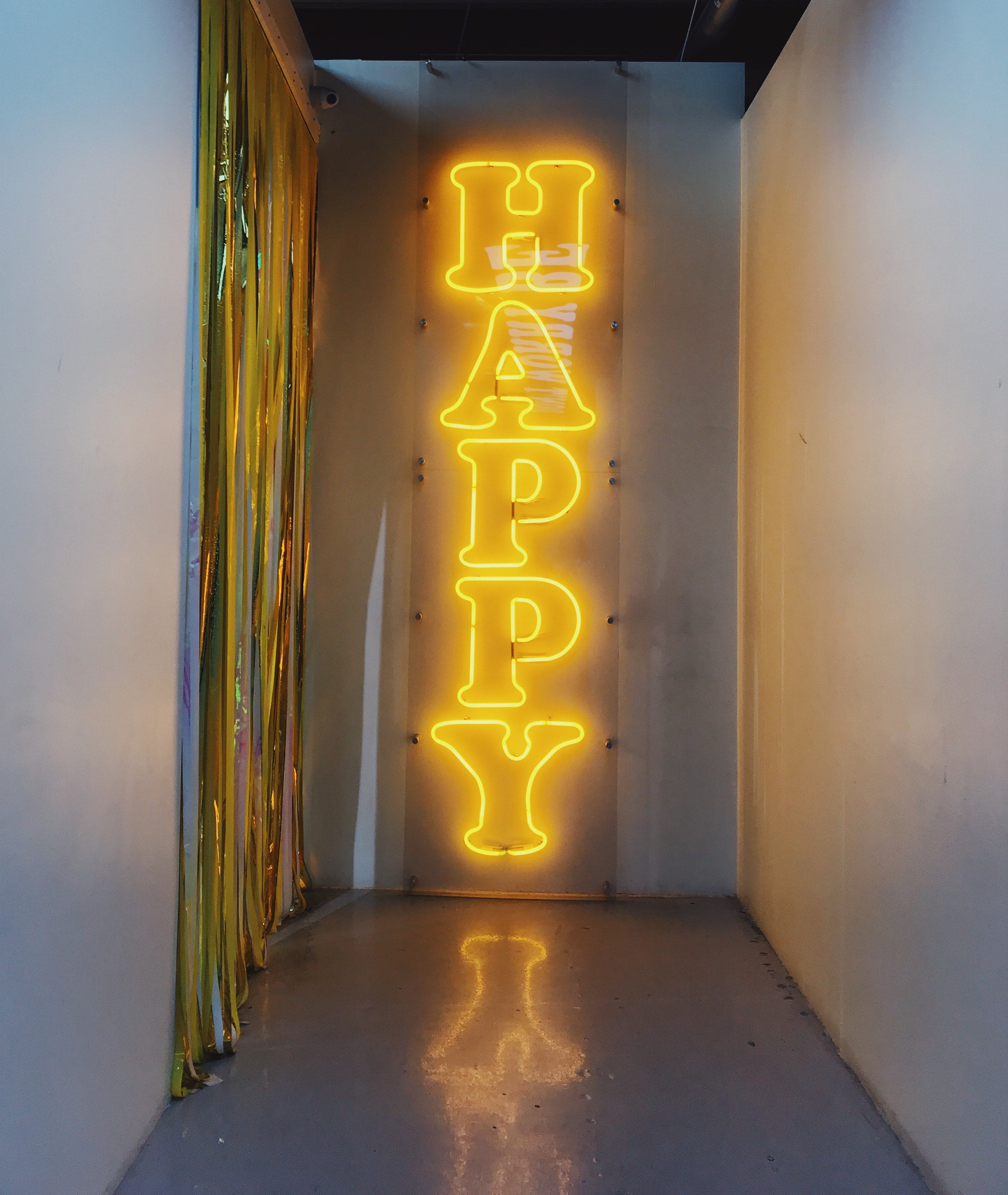 Yellow Neon Sign "Happy" on gray wall background. Brandi Ibrao - Unsplash