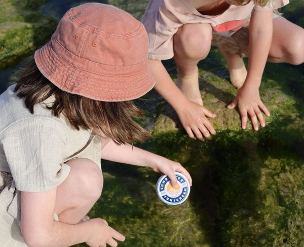 Things to look for in kids sunscreen - two children crouch beside a rock pool. One is holding a tin of SunButter sunscreen