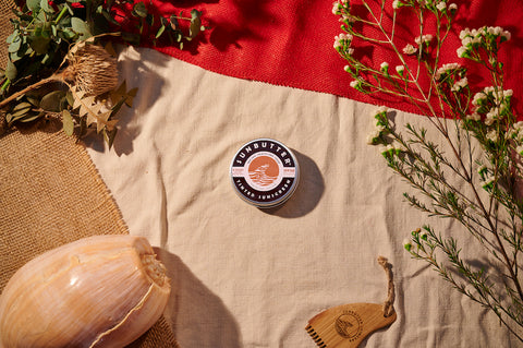 A tin of tinted SunButter sunscreen sits on a table surrounded by greenery 