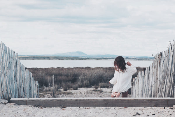 Windburn or sunburn? A small girl walks down some steps at the beach with an overcast sky overhead