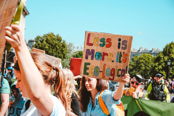 How can I reduce my emissions? A woman in a group of protesters holds a sign saying Less is More. It's Eco-logical