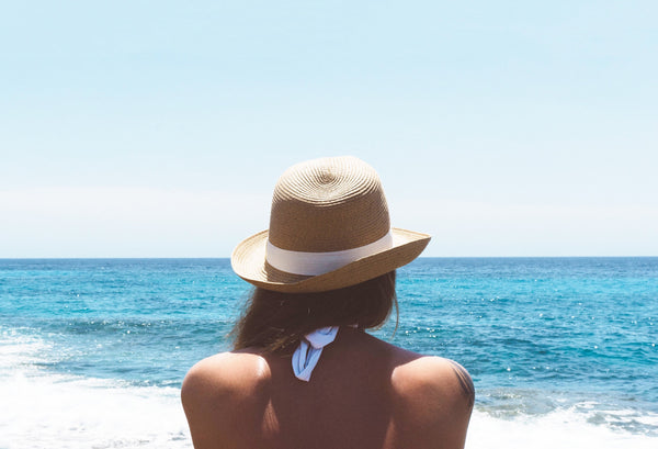 What is SPF and why is it important? Image of a woman wearing a hat and swimwear gazing out at a blue ocean and sky  
