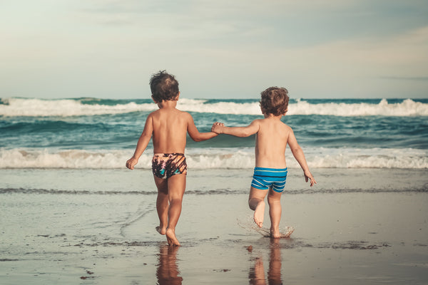 Five things to look for in kids sunscreen - Two young boys hold hands as they run towards the ocean