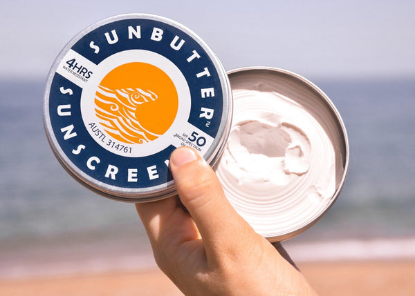 Ayurveda for skincare. An image of a hand holding a tin of sunscreen open so that you can see the white-coloured cream on the inside, as well as the surface of the tin, which reads, "SunButter Sunscreen". 