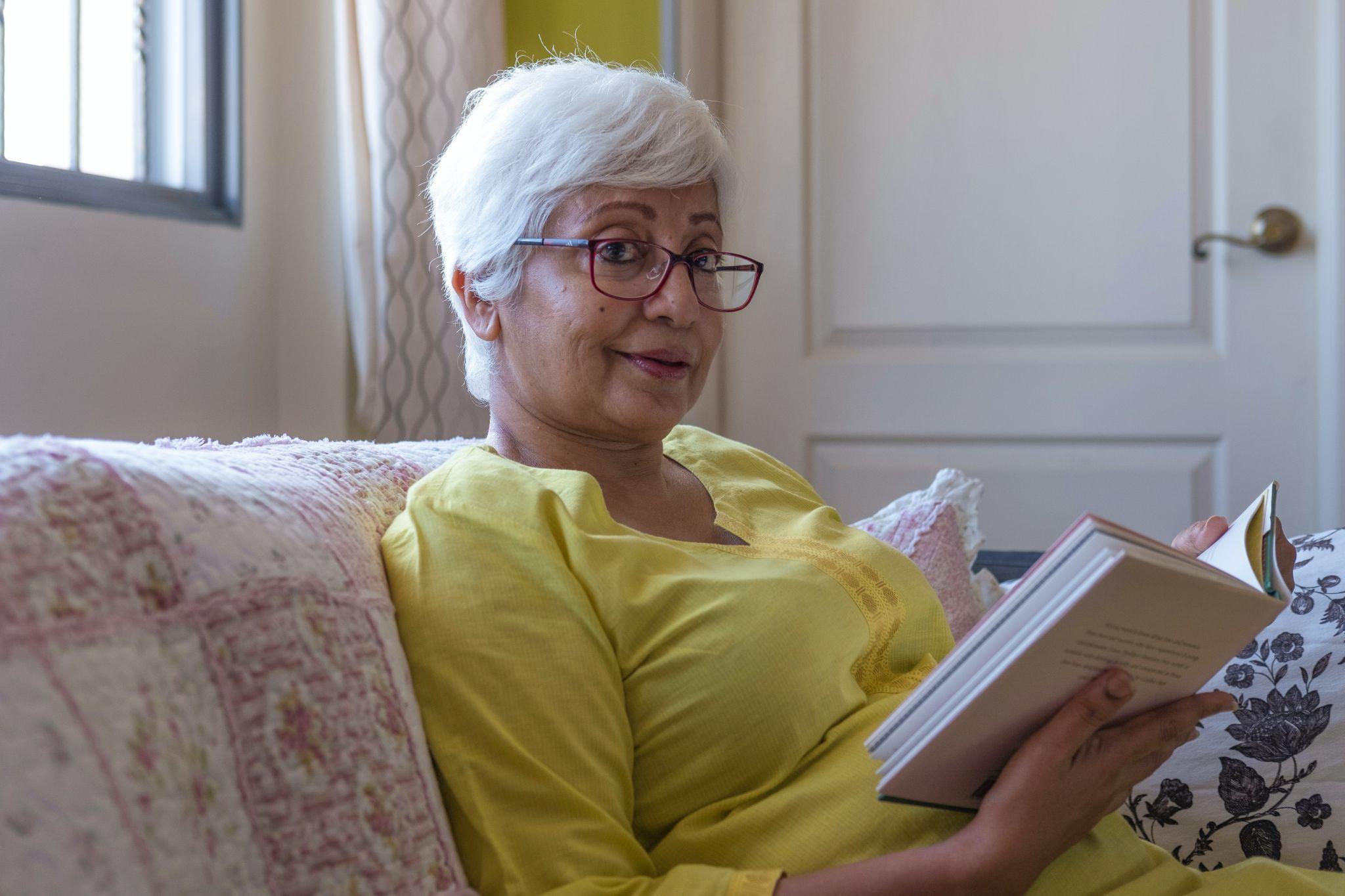 Senior woman sitting on a couch and reading a book.