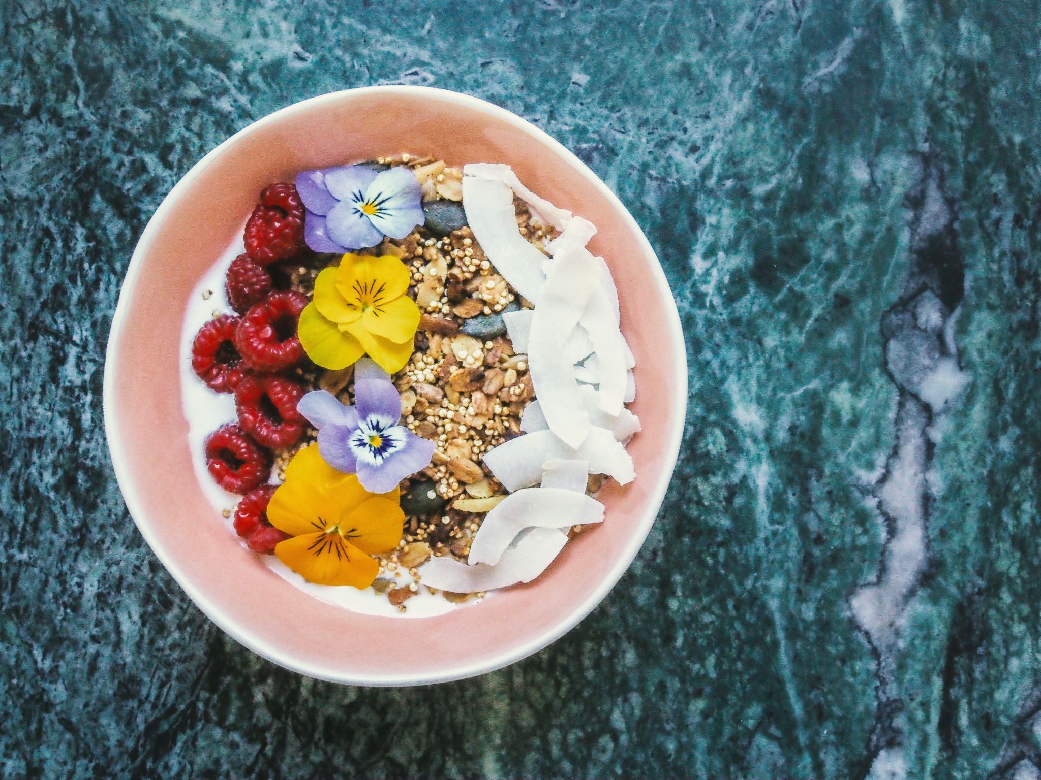 bowl with granola, raspberries, coconut flakes, flowers and milk.