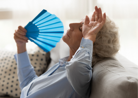 Tired woman suffering from heatstroke using a fan on the sofa