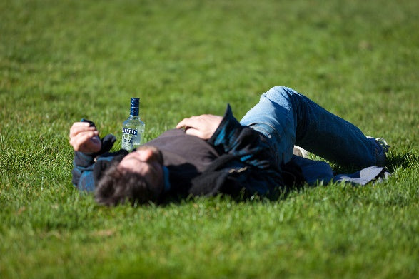 Man lying on lawn with a bottle of alcohol beside him