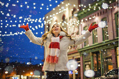 Happy woman with open arms looking at Christmas lights.