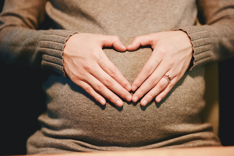 Woman with her hands in the shape of a heart over her pregnant belly