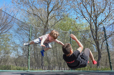 Two children jumping on a trampoline.