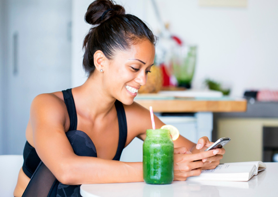 Woman drinking a green smoothie while checking her cell phone