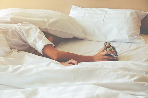 Woman sleeping in bed with alarm clock in her hand