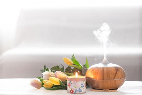 Various flowers, diffuser and lit candle on table.